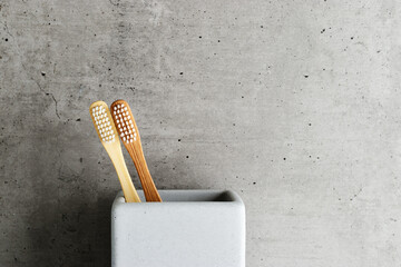 Eco-friendly wood toothbrushes with soft white bristles in modern grey concrete holder. Minimal...