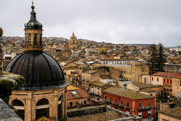 Panoramic View Over Ragusa From Cathedral Of San Giovanni Battista: Historic Sicilian City Rooftops, Church Domes, And Dense Stone Architecture Under Overcast Sky