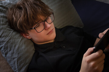 Unhappy stressed teenager boy lyuing down with smartphone
