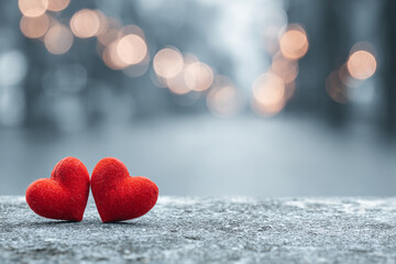 Fototapeta premium two fluffy red hearts sit on a textured grey surface with a soft focus background of glowing lights
