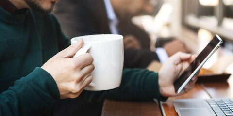 Man holding a large coffee mug while using a smartphone. Casual setting with focus on coffee and phone. Relaxed atmosphere with coffee and technology. A man in a coffee shop, drinking coffee.