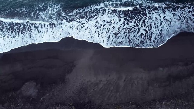 Aerial view of ocean waves crashing on a vibrant dark beach .4k Video.