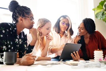 A diverse group of four women collaborate brainstorm around a table, sharing ideas and brainstorm...