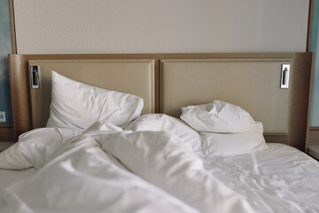 Unmade bed with white sheets and fluffy pillows, rumpled duvet creating a cozy, calm bedroom scene with soft light and inviting comfort