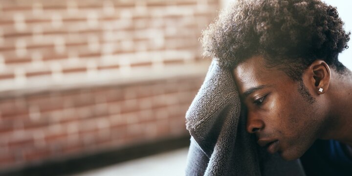 A person rests their head on towel, looking contemplative. The setting is against a brick wall, suggesting a moment of reflection or rest. African American man after exercising photo with copy space.