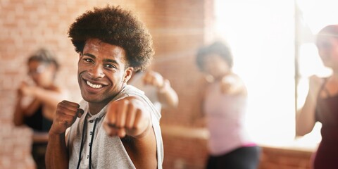 Smiling African American man in a fitness class, punching forward. The African American man is leading the class. Other participants follow the African American man's moves.