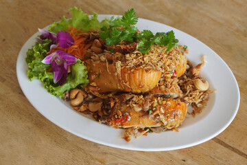 top view hot Stir-fried mantis shrimp with chili and salt In a white plastic dish, garnish with lettuce, strip Carrot and purple orchids, garnish with green coriander on a wooden floor background