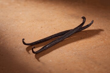 Two vanilla beans rest parallel on warm stone in calm minimalist still life