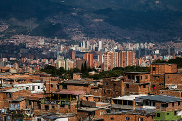 View of brick buildings cascade down the hillside towards a modern skyline under a sky, a vibrant tapestry of urban life, Medellin, Colombia.