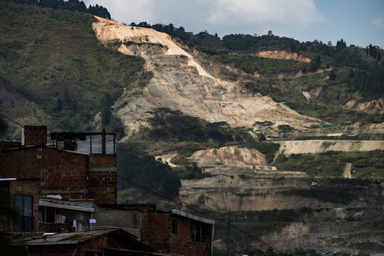 View of a dramatic mountainside scarred by quarrying behind a cluster of modest brick homes, a stark contrast of nature and industry, Medellin, Colombia.