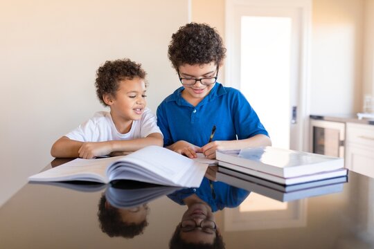 Two young boys studying together at a table at home. Books and learning materials are present. Students doing homework together after school. Education and knowledge. - Powered by Adobe