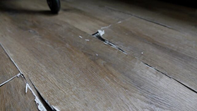 buckled laminate floor with torn planks and visible crack caused by heated floor expansion. closeup of damaged floor covering with lifted edges
