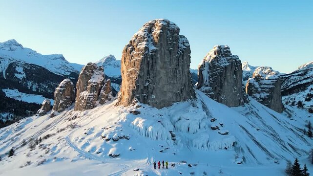 Five people stand dwarfed by towering, snow-dusted rocky peaks and icy slopes under a clear sky