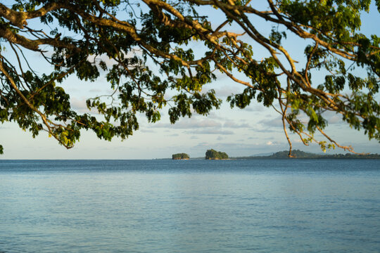 View of the calming sea, with distant islands framed by the overhanging tree branches creating a natural border, Vanimo, Sandaun Province, Papua New Guinea.