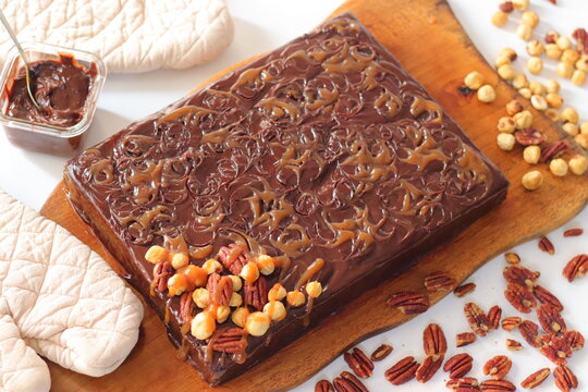 Chocolate caramel sheet cake with caramel drizzle and nut topping served on a wooden board