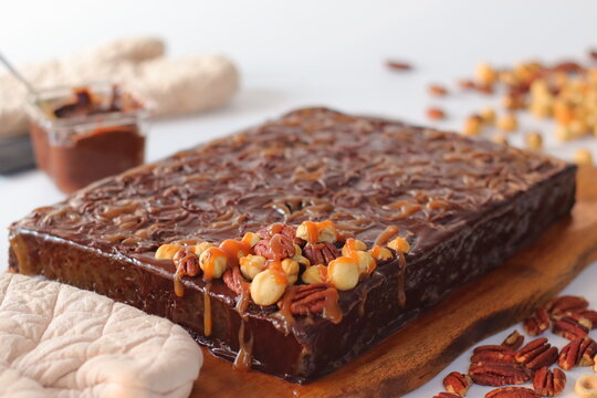 Chocolate caramel sheet cake with caramel drizzle and nut topping served on a wooden board