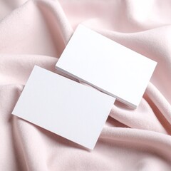 Two elegant white business cards are neatly placed on a soft, textured pink cloth, showcasing their clean design against the vibrant backdrop.