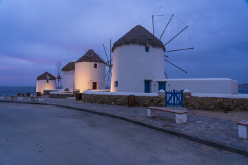 View of iconic whitewashed windmills stand majestically against the twilight sky, their thatched roofs and stone bases glowing softly, Mykonos, Mykonos, Greece.