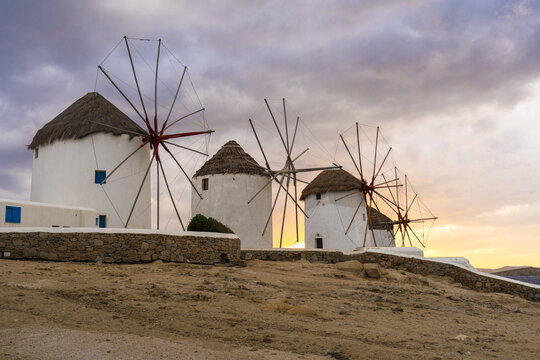 View of white windmills stand proudly against the dusky sky, their sails poised to catch the Aegean breeze, a timeless scene of Cycladic charm, Mykonos, Mykonos, Greece.