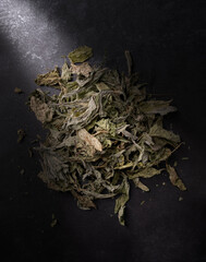 A pile of dried mint leaves in a strip of light on a black background