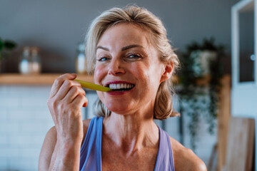 Smiling senior woman eating celery stick in kitchen: healthy lifestyle