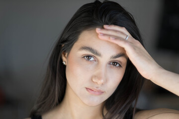 A woman with black hair wakes up in the morning in a white blanket and catches the rays of the sun. The portrait is creative, with brown eyes. High quality photo