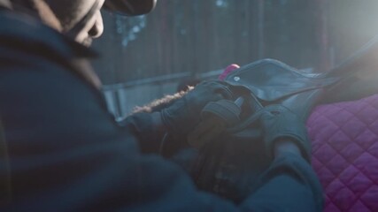 calm preparation scene before riding begins, focused rider finetuning tack under bright sunlight conditions, serene moment of saddle adjustment in natural light prior to equestrian activity