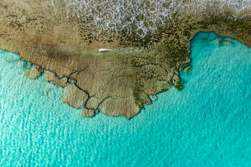 Aerial view shows fractured basalt shelves, turquoise shallows, small white breakers, tide pools, and mossy promontories near Playa del Bajo de la Burra in daylight.