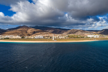 Aerial view shows Morro Jable beach, turquoise Atlantic, and the white Morro Jable lighthouse on...