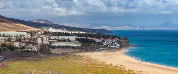 Terraced resorts and white and red villas sit on a cliff above Playa del Matorral, with the...