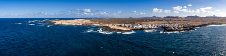 Aerial view of El Cotillo on volcanic rock and sandy coves in Fuerteventura, Canary Islands. Deep Atlantic water, foamy surf, arid plains, hills, and Lanzarote on horizon. © Aerial Film Studio