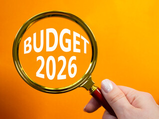 Budget 2026 symbol. Magnifying Glass with words Budget 2026. Beautiful orange background. Businessman hand. Business and Budget 2026 concept. Copy space.