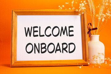 Welcome onboard symbol. Concept words Welcome onboard on beautiful wooden picture frame. Beautiful orange background with flower vase. Business and Welcome onboard concept. Copy space.