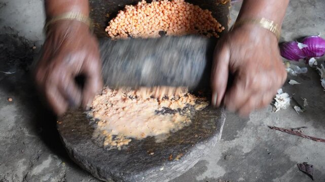 Person grinding ingredients on traditional stone slab with roller