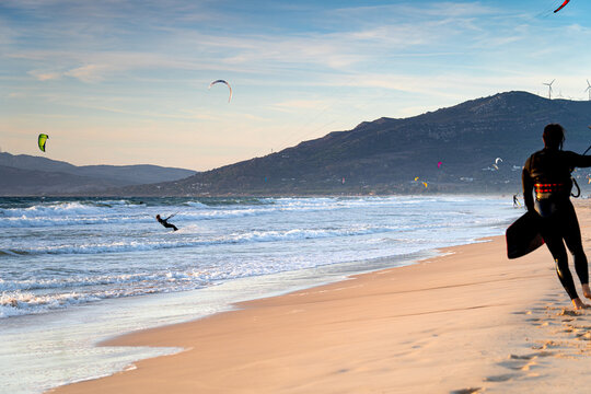 Kitesurfer with a board walks along the coast at sunset holding a kite, Tarifa surf spot, Spain