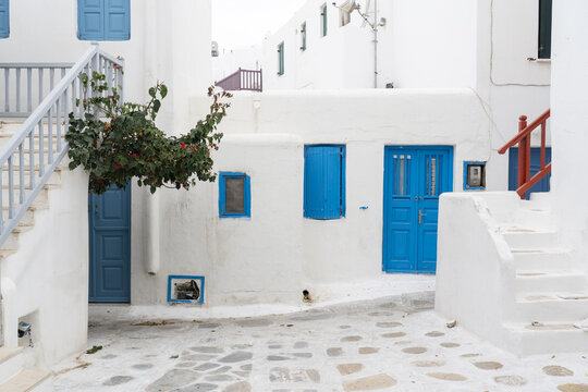 View of bright blue doors and window frames contrast against the stark white walls of buildings in a narrow cobblestone street, Mykonos, Greece.