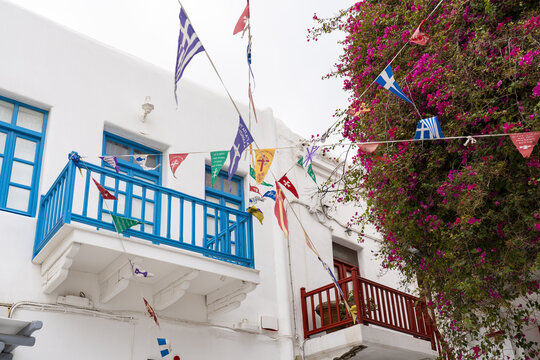 View of white-washed buildings adorned with vibrant flags and hot pink bougainvillea, creating a striking contrast in the old town, Mykonos, Greece.