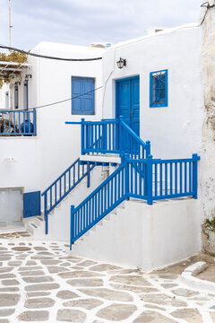 View of brilliant blue railings and window frames accenting a pristine white building on a stone-paved street in Old Town, Mykonos, Greece.