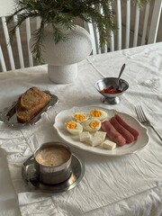 Minimal breakfast flat lay with boiled eggs, sausages, cheese, toast, red caviar, and coffee on white linen tablecloth, styled in cozy Scandinavian winter mood.