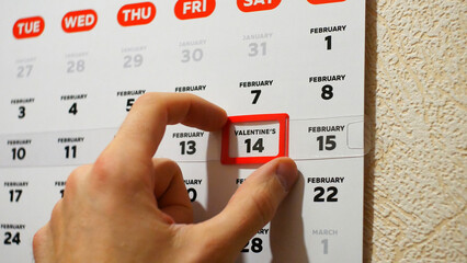 Close-up of male hands moving a wall calendar red cursor to the date of Valentine's Day