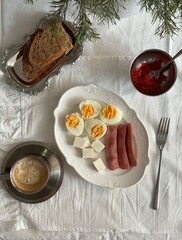 Minimal breakfast flat lay with boiled eggs, sausages, cheese, toast, red caviar, and coffee on white linen tablecloth, styled in cozy Scandinavian winter mood.