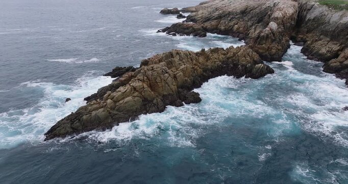 Aerial drone flight along Coruna rocky coastline, Galicia, Spain, showcasing Atlantic waves, rugged cliffs and textured sea foam patterns