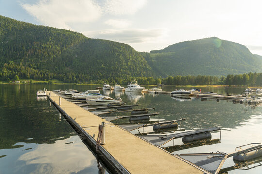 View of serene waters reflecting the sky, boats gently moored along the pier, and forested hills in the distance, creating a tranquil scene, Dalen, Telemark, Norway.