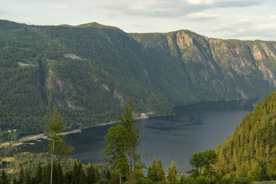 View of deep blue waters reflecting the towering, tree-covered mountains under a soft sky in the Norwegian landscape, Dalen, Telemark, Norway.