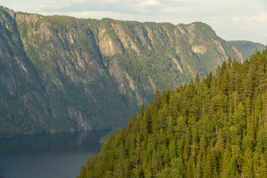 View of the rugged, forested mountains plunging into the still, dark waters of a lake, a scene of natural grandeur and serene beauty, Dalen, Telemark, Norway.