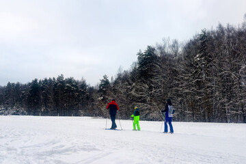 Family of cross-country skiers (dad, mom and little child) in the snowy winter park. Side view. Sports and active lifestyle concept