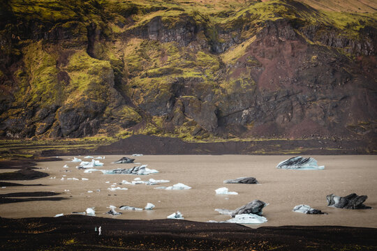 View of floating icebergs drift on the glacier lagoon, reflecting the sky, surrounded by rugged mountains, creating a serene yet powerful scene, South Island, Iceland.