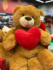Cute teddy bear holding a red heart displayed in a store. Soft plush toy symbolizing love, affection, romance, and gift ideas for holidays, celebrations, and emotional moments.