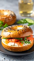 Salmon, cream cheese, and cucumber bagel sandwich on a black plate, with another bagel and liquid in background