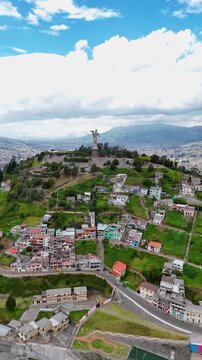 Vertical aerial drone footage of El Panecillo hill featuring the Virgin of Quito statue overlooking the city of Quito, Ecuador.